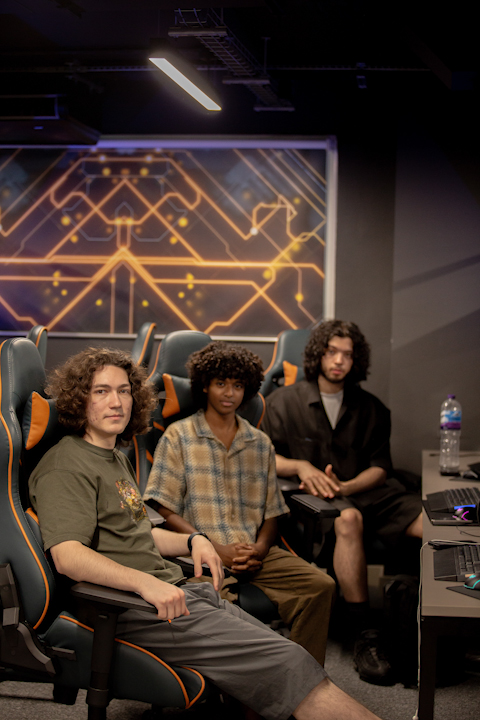 3 young developers, the team members of the team CTRL ALT X, sat at a desk on gaming chairs while facing the camera with a neutral expression