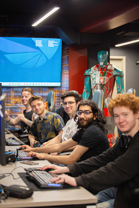 5 young developers, the team members of the team TLDR, sat at a desk on gaming chairs while facing the camera, smiling, and giving thumbs-up gestures